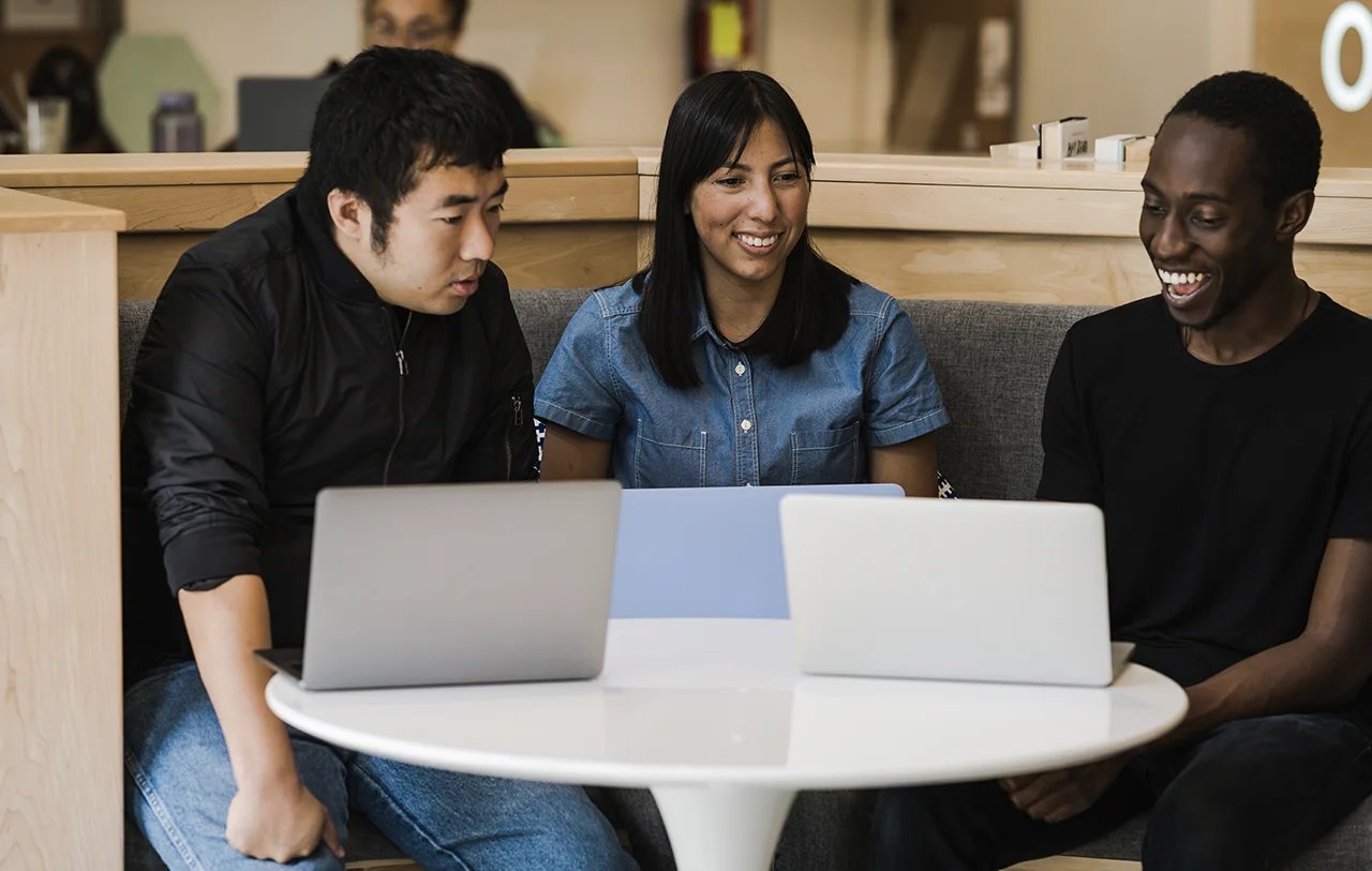 Drei Teammitglieder, die mit ihren Laptops an einem Tisch arbeiten
